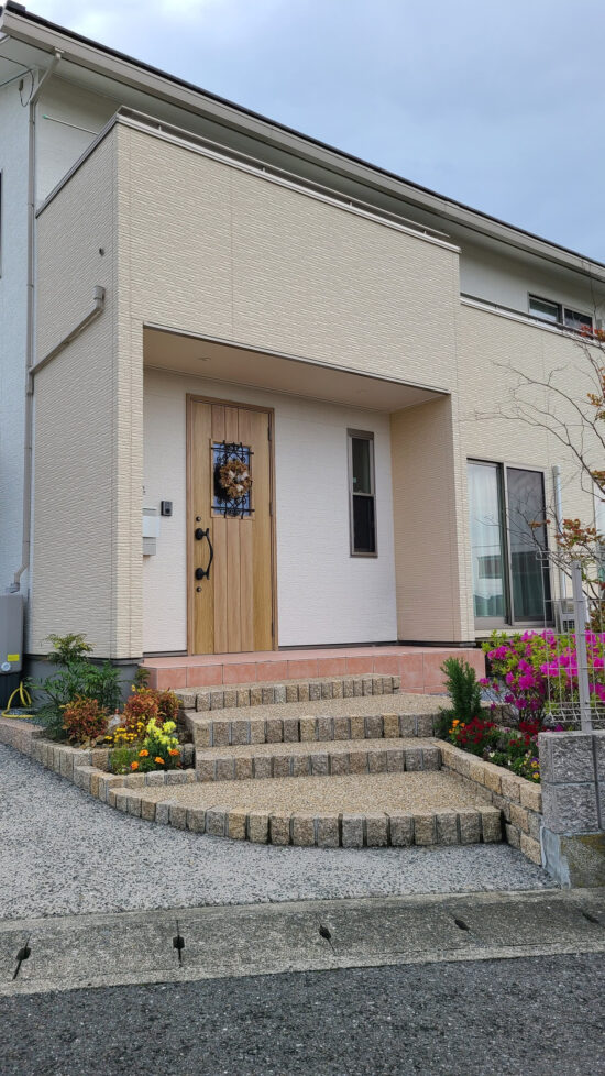 四季の花が咲くアプローチとナチュラルデザインの二階建て住宅外観