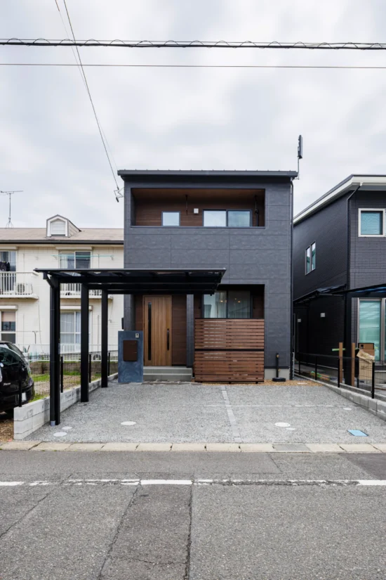 ダークグレーの外壁と木目アクセントが映えるシンプルモダンな二階建て住宅外観